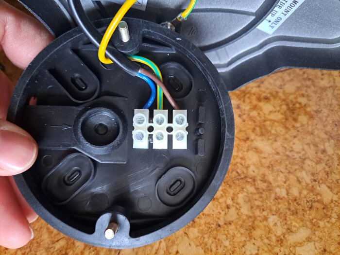 Elektrisk kopplingsplatta med flera färgade kablar: gul/grön, blå och brun, anslutna till en ny lampa, på en kritfärgad yta.