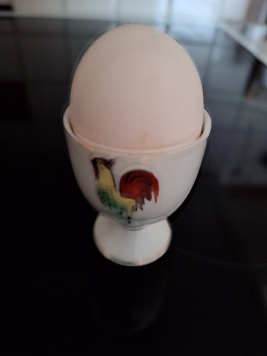 Ägg i äggkopp med tuppmotiv på mörk yta.