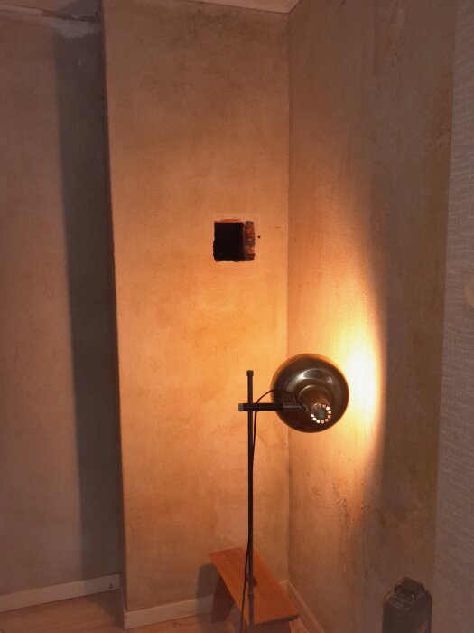 Vägg med ett fyrkantigt hål, upplyst av en golvlampa. Hålet är öppet i en murstock för installation av en ny kamin.