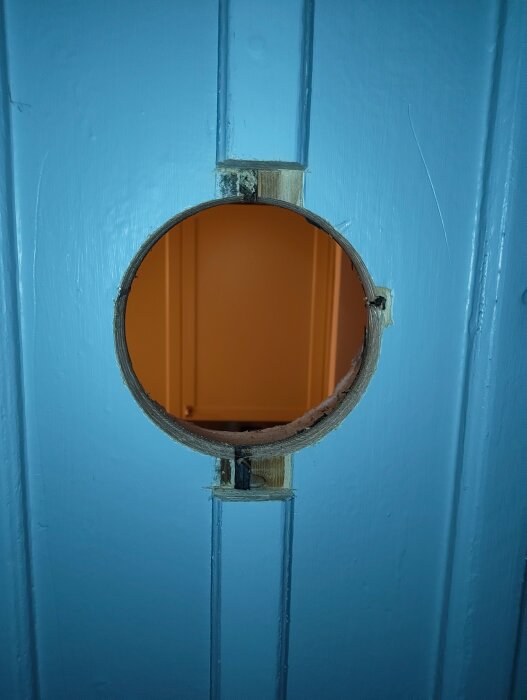 Runt hål sågat i en blåmålad ytterpanel för installation av spirorör och brandisolering.