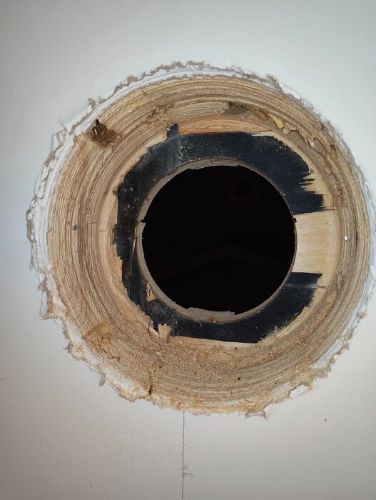 Hål i vägg för spirorör och isolering, del av installation med brandspjäll och ytterhuva. Visar snittytor i trä och vägg, omkringliggande bräckt material.