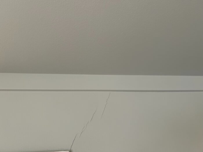 Sprickor i väggen nära taket, synliga längs taklisten i ett nyrenoverat rum.