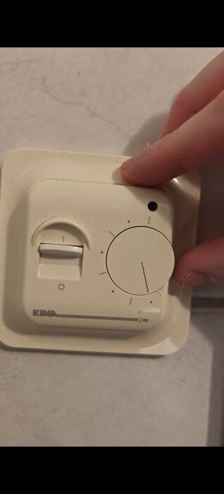 KIMA termostat installerad på vägg, justeras med hand.