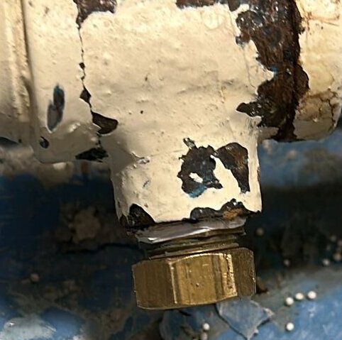 Närbild av rostig vit och blåmålad rörkoppling med metallmutter, sliten färg som flagnar.