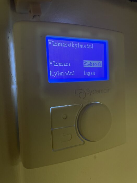 Systemairs kontrollpanel med blå skärm visar inställningar för värmare och kylmodul, där "Elektrisk" är valt för värmaren och "Ingen" för kylmodulen.