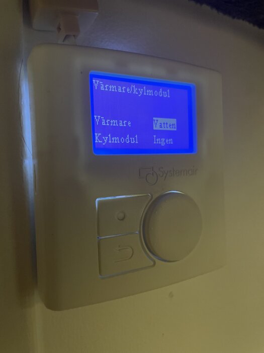 Termostat med ljusblå skärm, visar alternativ för värmare och kylmodul med valen "Vatten" och "Ingen". Systemair-logotyp synlig.