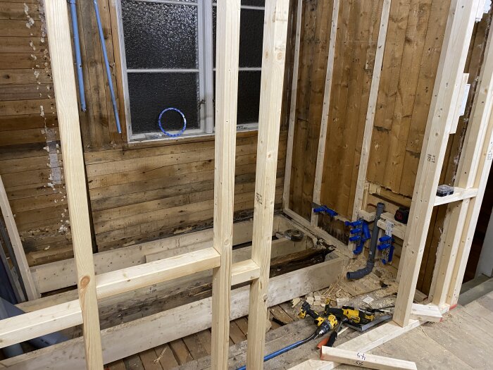 Träreglar och VVS-installation i ovanvåningens renoveringsprojekt, med synlig borrmaskin och arbetsmaterial framför ett gammalt fönster.