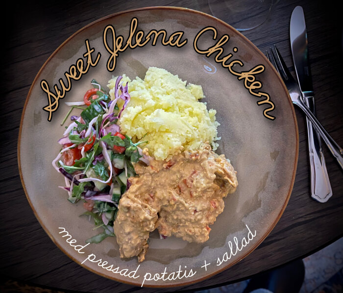 En tallrik med Sweet Jelena Chicken, pressad potatis och sallad. Bestick ligger bredvid på ett mörkt träbord.