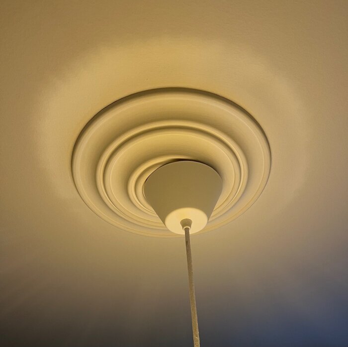 Takrosett med lampa; sladden är ej centrerad vilket gör att takkopp sitter snett mot rosetten.