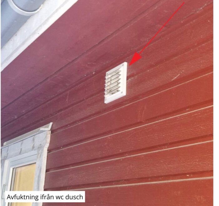 Badrumsfläkt under takfot med röd fasad, vit ventilation och pil markerar uttaget.