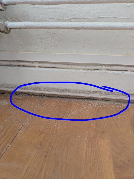 Mellanrum på 1,5 cm vid golv efter borttagning av spånskiva med vinylmatta, markerat med blå cirkel, synliga lister och rör ovanpå.