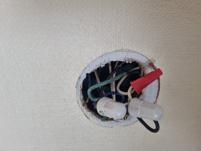 Öppen elinstallation med exponerade kablar och tre kopplingar, varav en röd trådmutter.