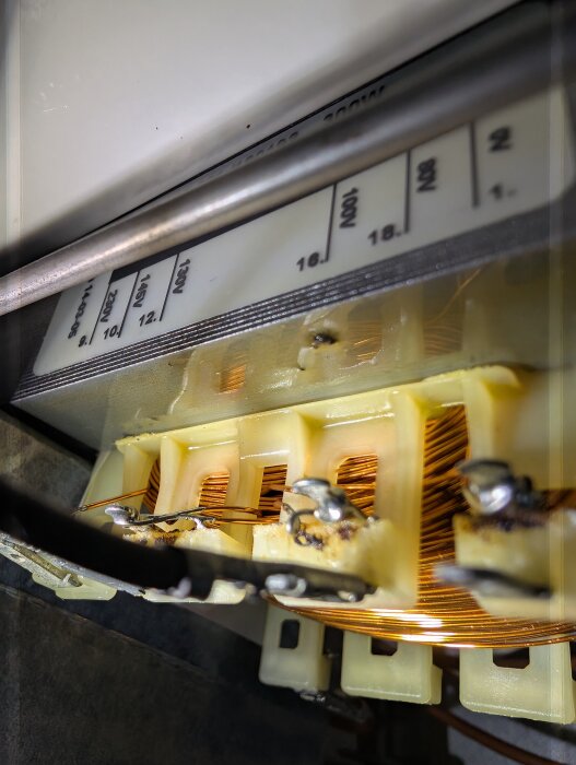 Närbild av en elektrisk lindning med koppartråd och anslutningar, med en märkplatta ovanför som visar olika spänningssteg.