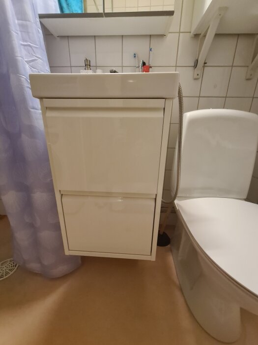 Vitt badrumsskåp med handfat ovanpå, intill en toalett, ingen omdragning av rör.