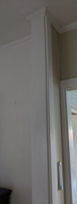 Öppning där en vägg tidigare stod, med kvarvarande del av dörrkarm och väggbeklädnad, som syns mot taket och en termostat på väggen.