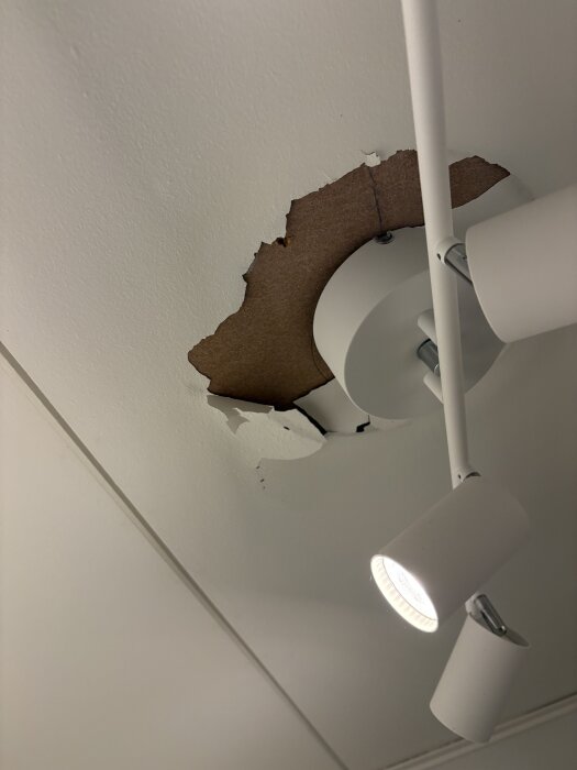 Tak med avflagnad färg, exponerade råa takplattor runt en nedtagen taklampa.