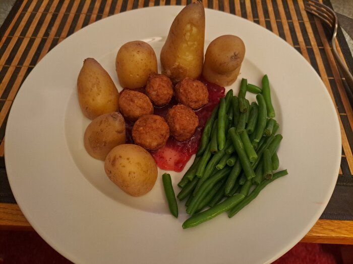 Potatis, köttbullar med sås och haricots verts på en vit tallrik.