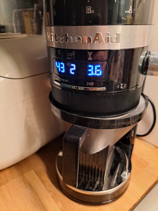Svart kaffekvarn från KitchenAid stående på en bänkskiva, med filterhållare och blå lysande display som visar inställningar.