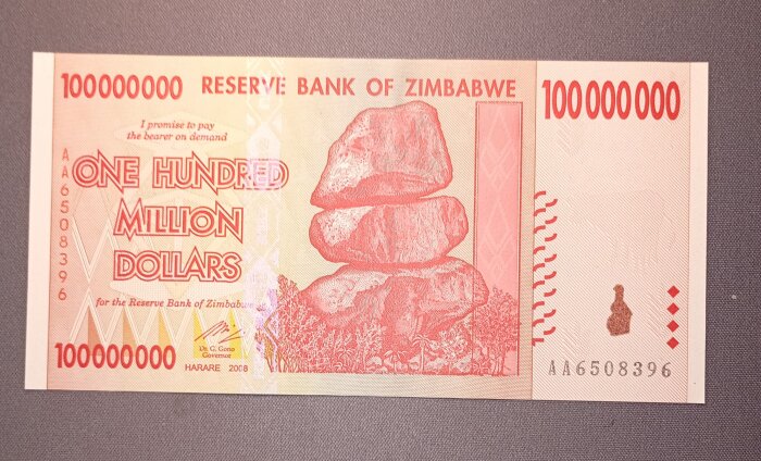 En 100 biljoner Zimbabwe dollar-sedel med staplade stenar och träd i rött tryck.