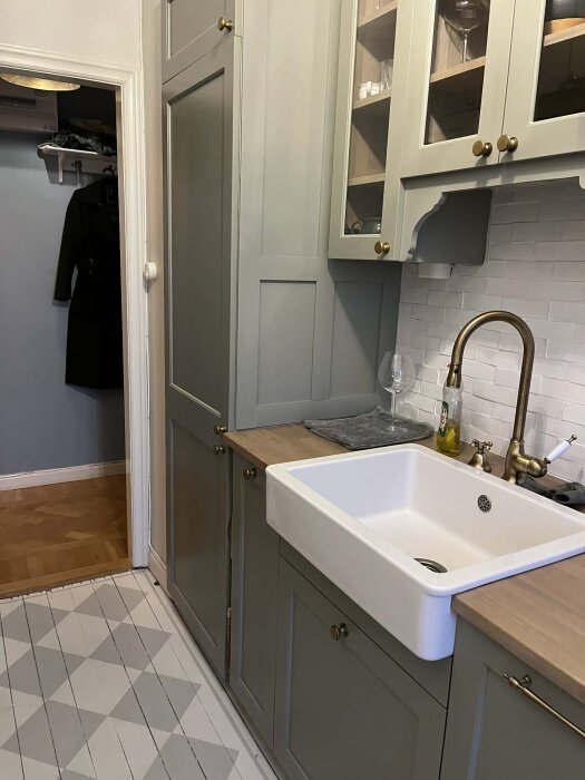 Grönt kök med diskho och överskåp, där tanken är att installera ventilationsgaller ovanför kylskåp för bättre ventilation.