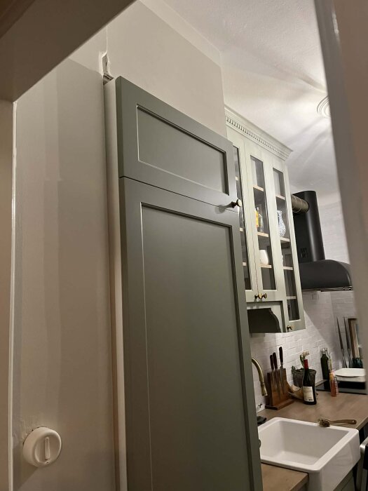 Kök med grön skåpdörr ovanför diskbänk, föreslaget område för ventilationsgaller i diskussion om kylskåpsventilation.
