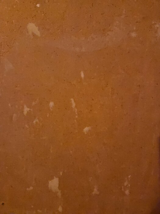 Brun vägg med ojämn yta och ljusa fläckar, potentiellt masonitskiva under gammal tapet, del av renoveringsprojekt.