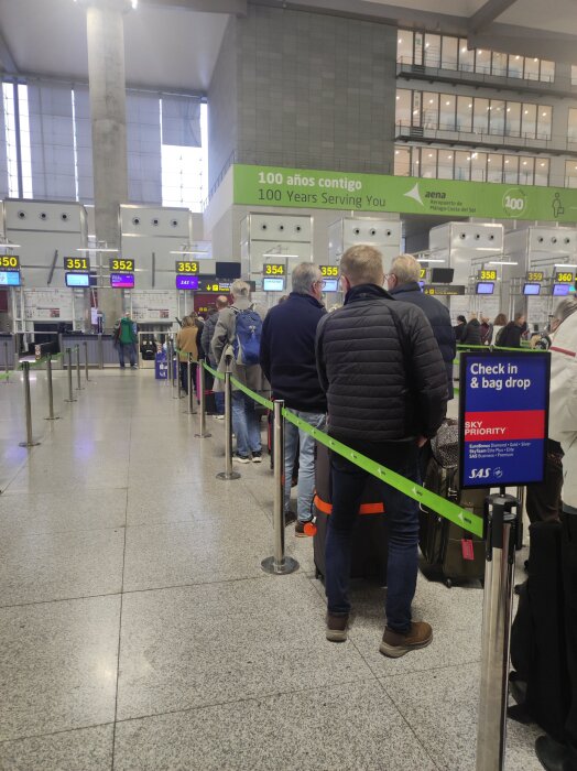 Personer står i kö vid incheckning och bag drop vid en flygplats, skylten visar "Sky Priority".