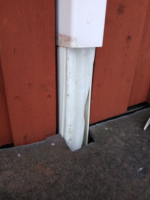 Dräneringsrör vid röd trävägg, del av luft-luft värmepump, synligt problem med isbildning orsakat av varierad drift av värme och AC.