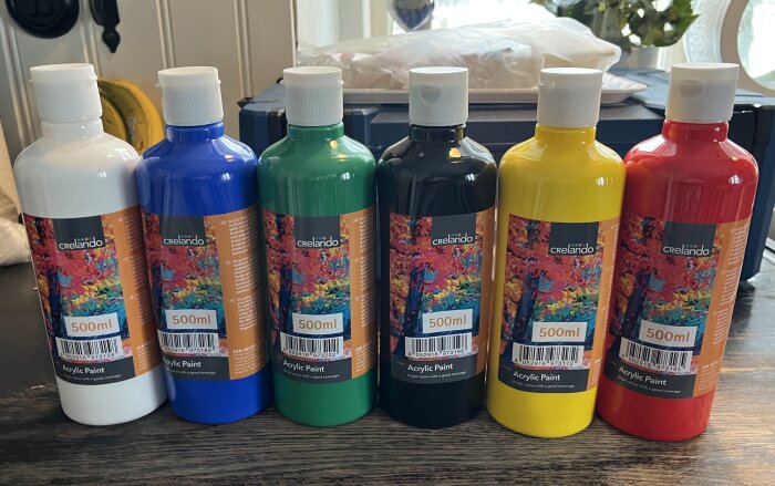 Sex flaskor akrylfärg på ett bord i färgerna vit, blå, grön, svart, gul och röd. Flaskorna är märkta med 500 ml.