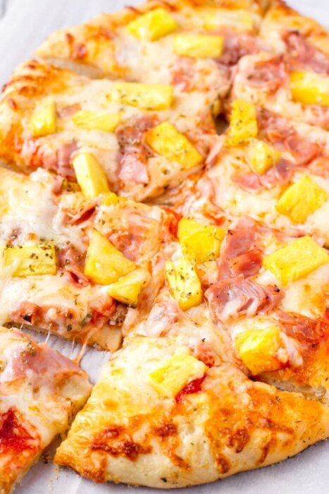 Pizza med ananas och skinka, ofta känd som Hawaii-pizza, med smält ost och skivad i delar.