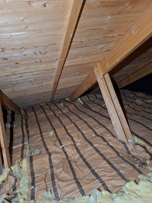 Loft med träunderlag, papp och isolering. Vinklat tak syns, och användaren är osäker på luftspalter vid takfoten.