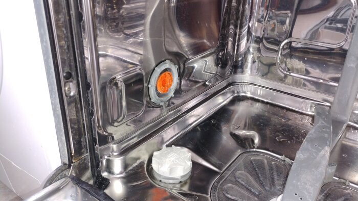 Insidan av en diskmaskin med en lös plastmutter nära vattenmjukgöraren, orsakar droppande och läckageproblem.