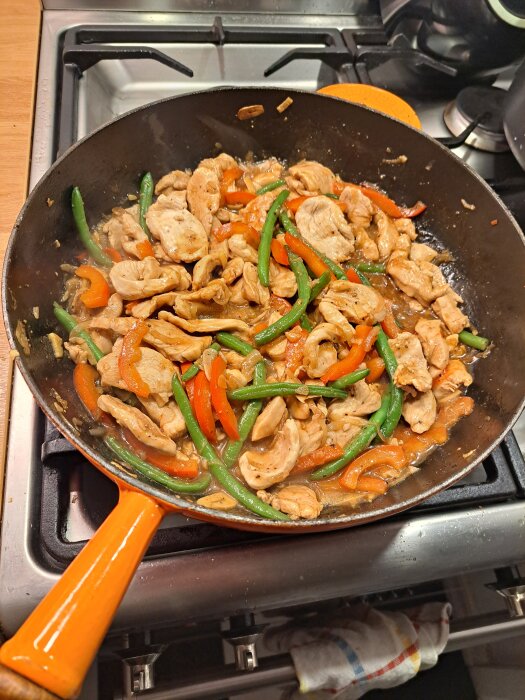 Kycklingwok med paprika och gröna bönor i en stekpanna på en spis.