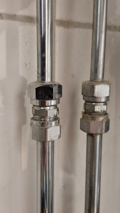 Närbild på två metallrör och deras kopplingar i ett badrum, i samband med installation av ny blandare.