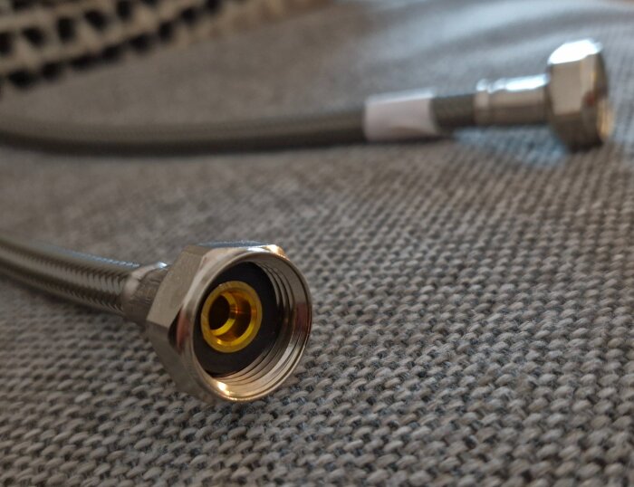 Flexislang med metallanslutning och gängor placerad på en grå textil yta.