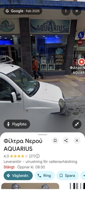 Butiken "AQUARIUS" med skyltar, en parkerad bil och en person som går förbi på trottoaren framför.