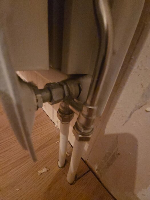 Radiatoranslutningar mot trägolv utan synlig ventil för utlopp.