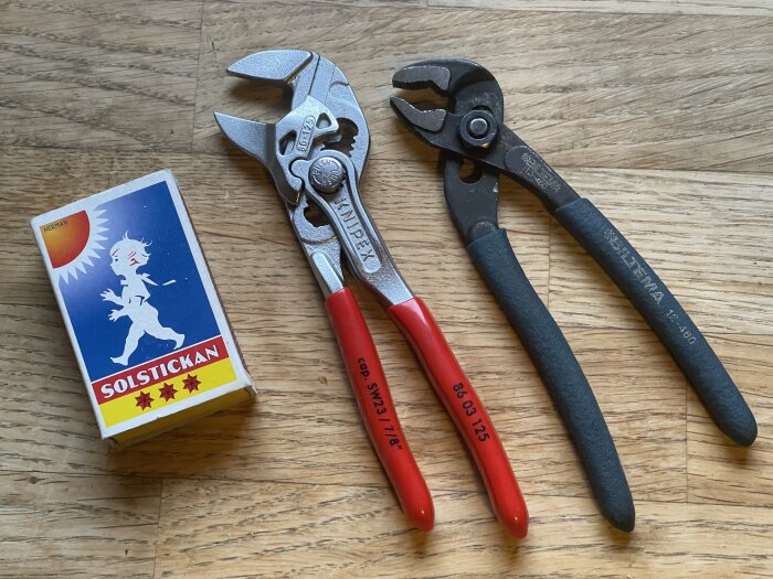 En tändsticksask bredvid två tänger; en röd- och silverfärgad muttertång och en svart polygrip.