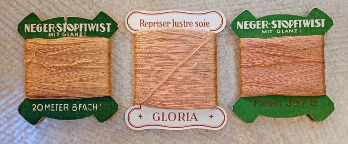 Vintage stoppgarn hållare, inklusive "Neger-Stopftwist mit Glanz" och "Gloria" etiketter i beige nyanser, symbol för hållbarhet och gammalt hantverk.