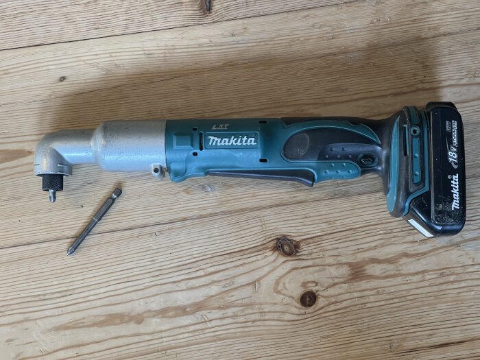 Makita LXT slagskruvdragare med 18V batteripack ligger på ett trägolv, bredvid ett löst bits.