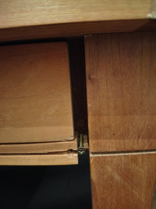 Närbild på ett skrivbord där en skruv är delvis lös och en synlig spricka indikerar en skadad del på träet.