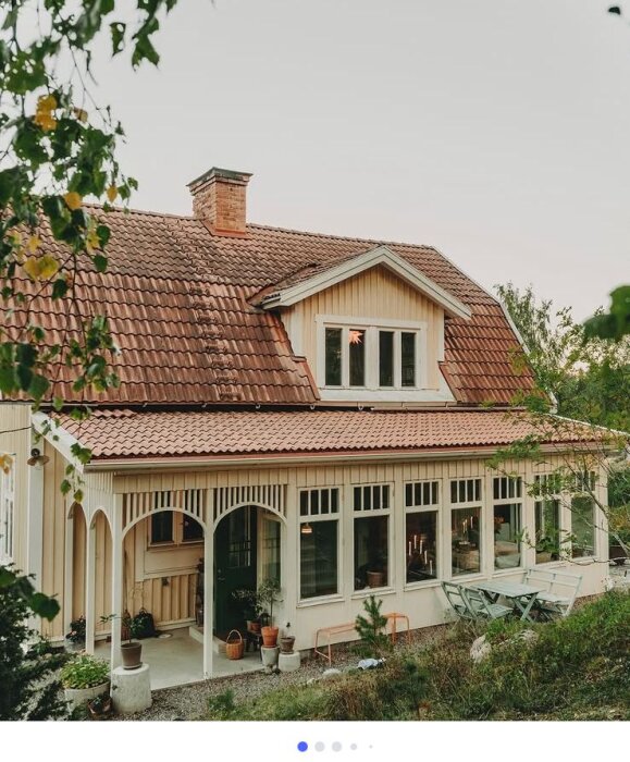 Gammalt hus med tegeltak, verandor och många fönster, omringat av grönska.