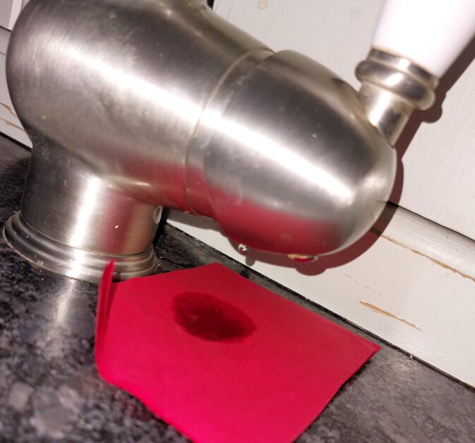 Droppande köksblandare i antiksilver med röd bit papper som absorberat vatten på diskbänken.