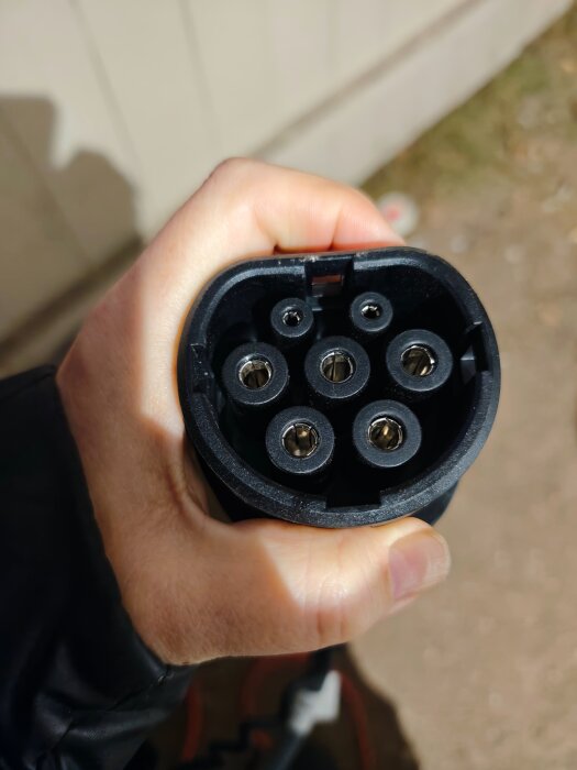En hand som håller en elbilsladdare med flera stift, utomhus.