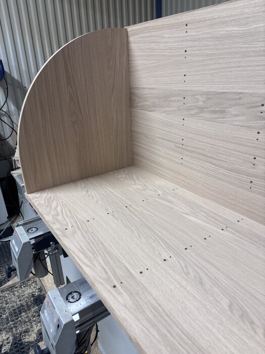 Träpanel för projekt med svängda luckor, monterad på underlag med maskiner, visar monteringshål och böjda former.
