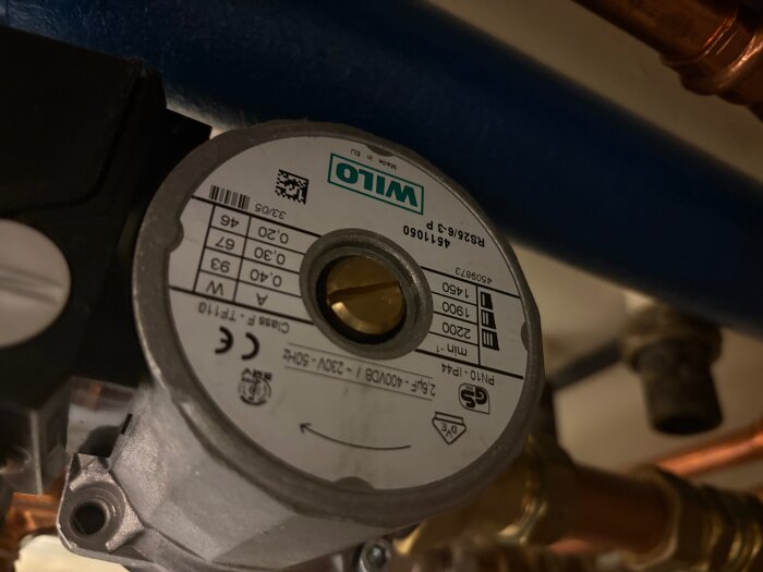 Cirkulationspump av märket Wilo med specifikationer på etiketten, omgiven av rör och ventilationsdetaljer.