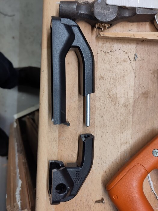 Trasigt handtag från lådcykelbatteri delat i två, liggande på träbord bredvid en hammare och en multisåg.