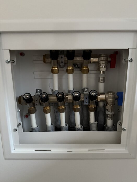Central radiatorfördelare med flera ventiler och rör, del av vattenburen golvvärmeinstallation i huset för temperaturkontroll.