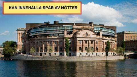 Byggnad vid vattnet med text "KAN INNEHÅLLA SPÅR AV NÖTTER" i överkant.