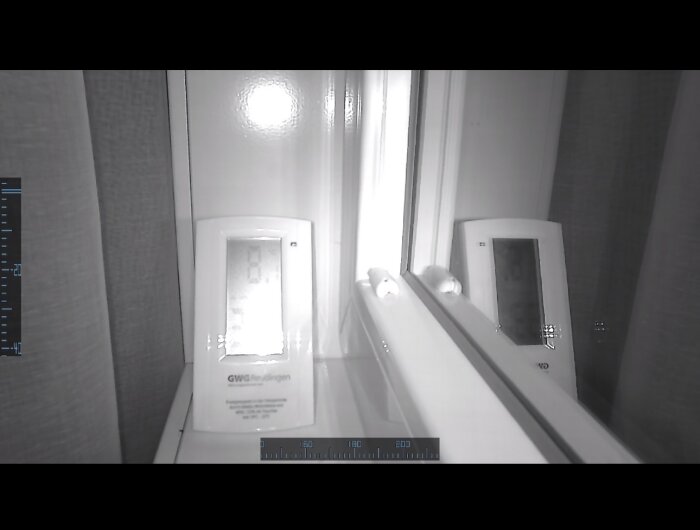 Termostat från GWG Reutlingen syns i spegelbild vid fönster, med en avläsning på skärmen.